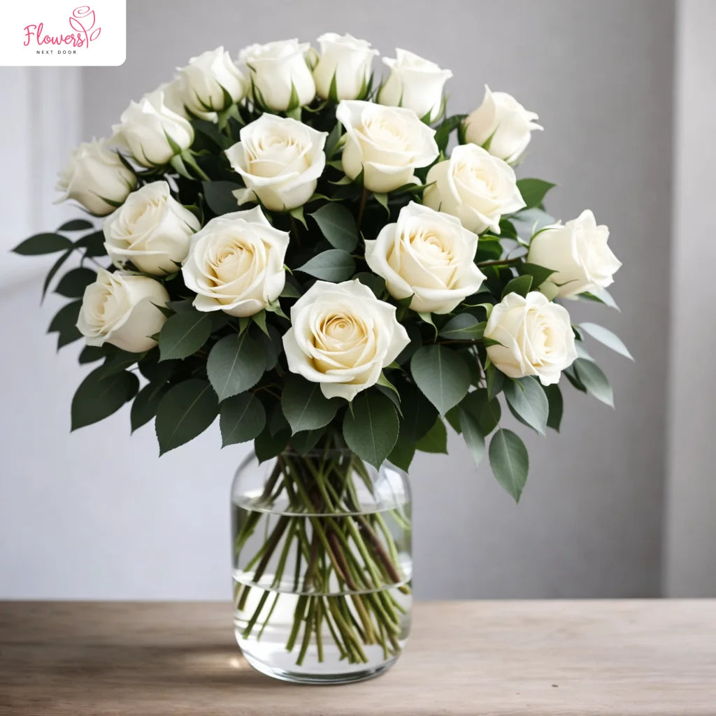 Bouquet of white roses in a clear vase on a wooden table with a neutral background