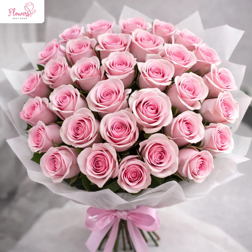 Bouquet of pink roses with a pink bow on a light gray background, featuring the 'Flowers Next Door' logo.