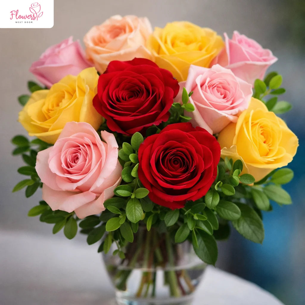 Bouquet of red, yellow, and pink roses in a clear vase on a blurred background.