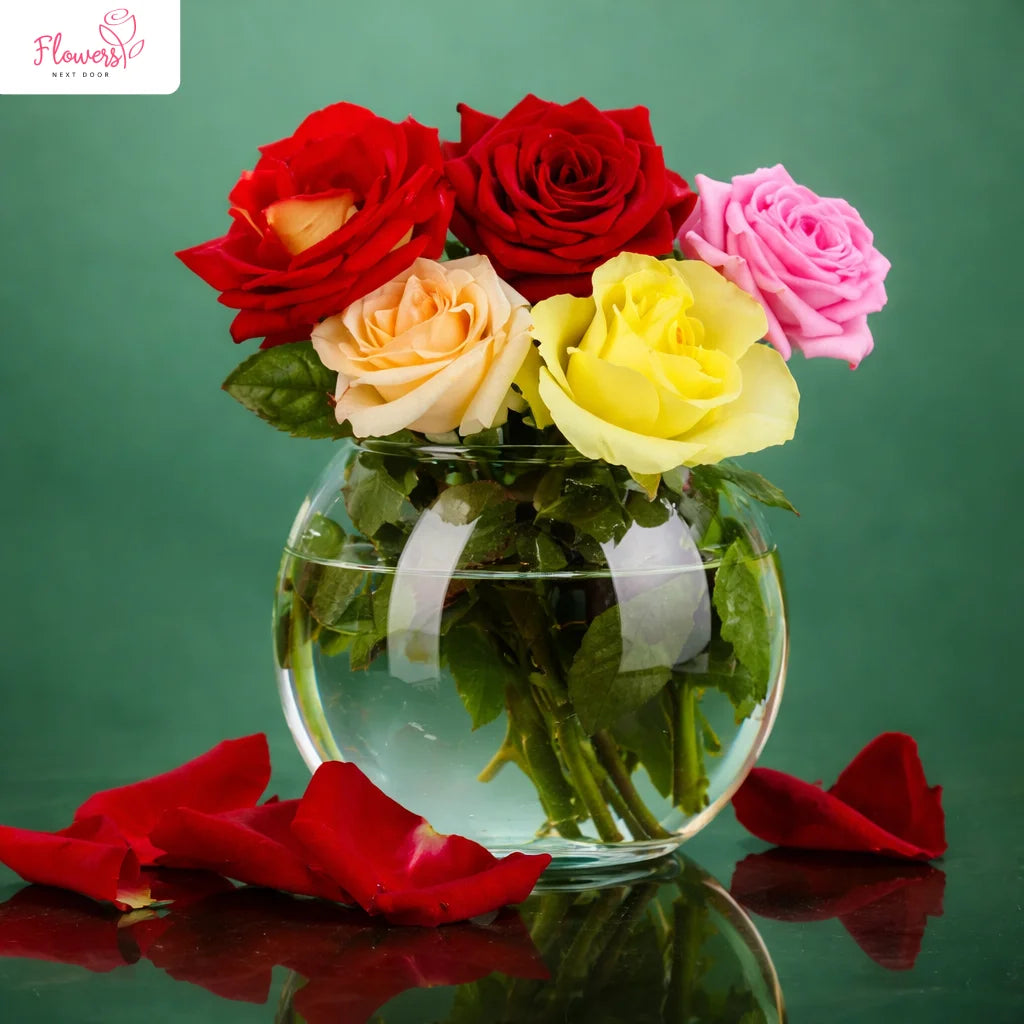 Clear glass vase with colorful roses on a reflective surface with a green background